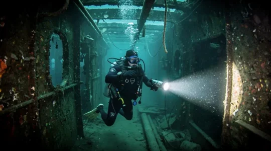 Plongeur explorant l'intérieur d'une épave sous-marine en utilisant une lampe de plongée principale pour éclairer les structures métalliques dans l'obscurité